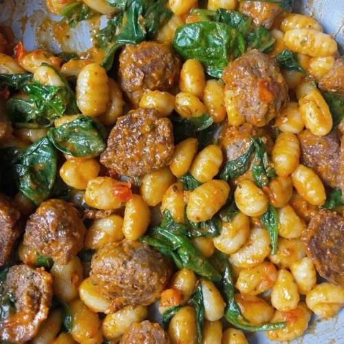 Plate of gnocchi meatballs with spinach topped with grated cheese.