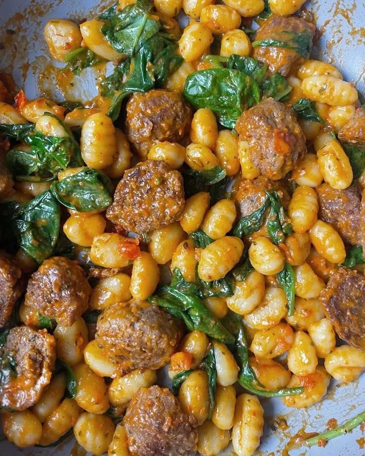 Plate of gnocchi meatballs with spinach topped with grated cheese.